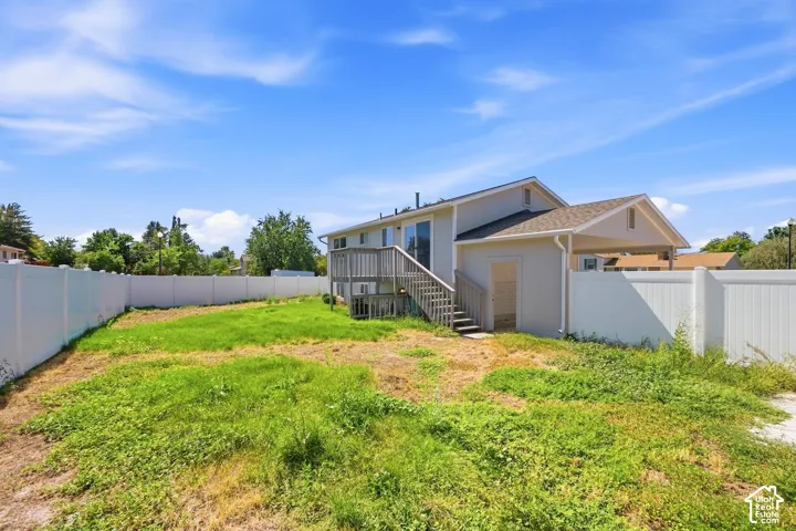 Expansive outdoor space featuring a two-story residence with a second-level deck, ground-level access, and a covered carport, all enclosed by a white privacy fence