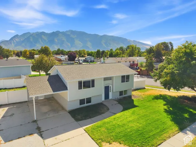 Split-level residence featuring a carport, front lawn, mountain scenery, and a paved driveway