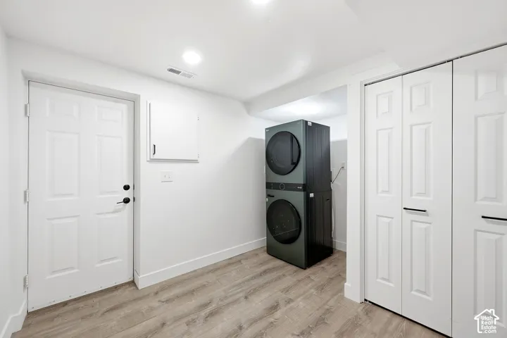 Laundry area featuring a stacked washer and dryer, wood-finish flooring, recessed lighting, and white bi-fold closet doors
