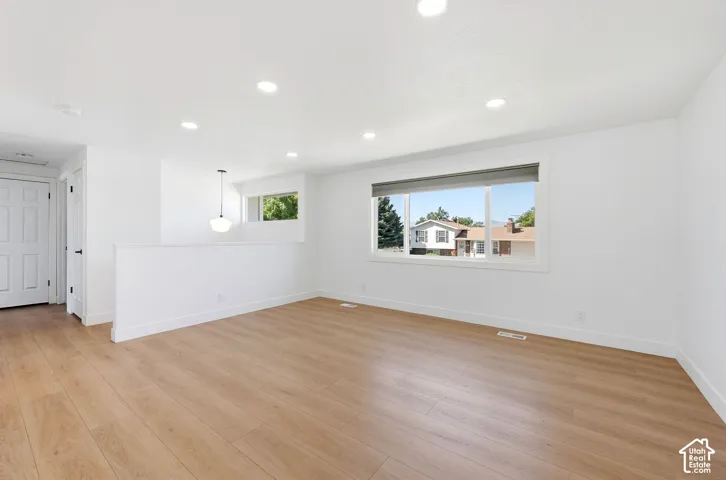 Expansive room featuring wood-finish flooring, white walls, recessed lighting, a large window, and a white paneled door