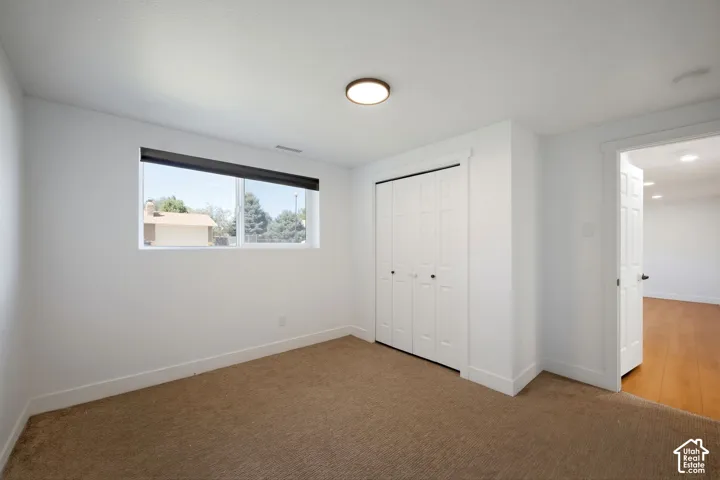 Carpeted room with a single window, white walls, and bi-fold closet doors