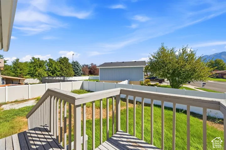 Exterior deck with wood-finish railing, overlooking a fenced yard and mountain backdrop