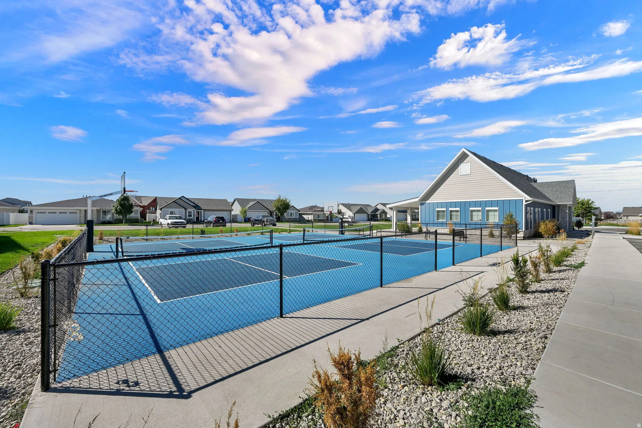 Community clubhouse with multiple outdoor courts, surrounding rock landscaping, and paved pathways