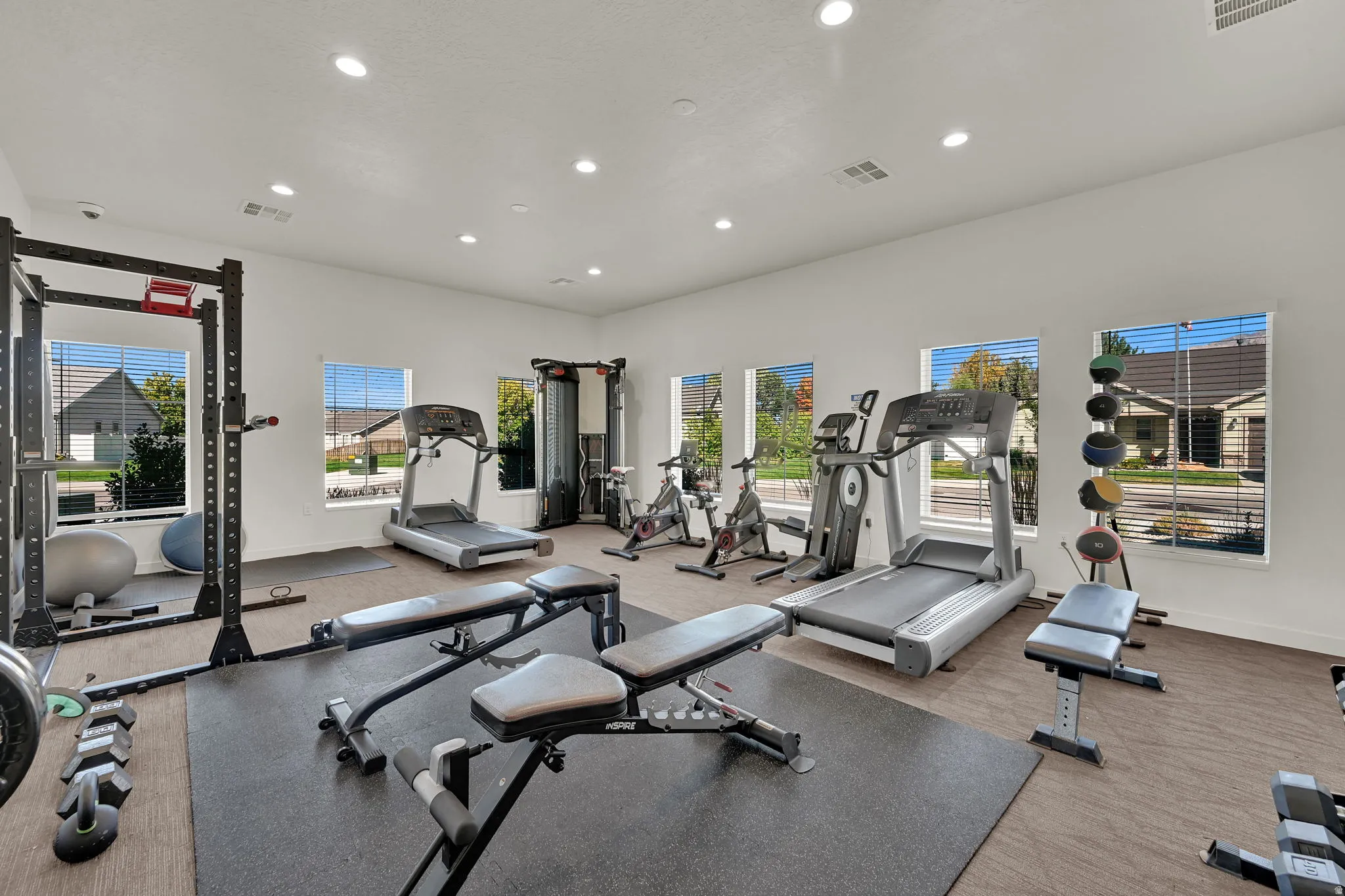 Dedicated fitness room featuring recessed lighting, multiple windows for natural light, diverse gym equipment and  rubber mats.