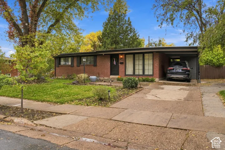 Single-story brick exterior featuring a flat roofline, attached carport, multi-pane windows, and mature landscaping