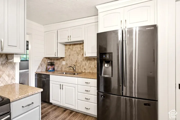Kitchen featuring white cabinetry, stone countertops, a patterned stone backsplash, stainless steel appliances, and wood-finish flooring