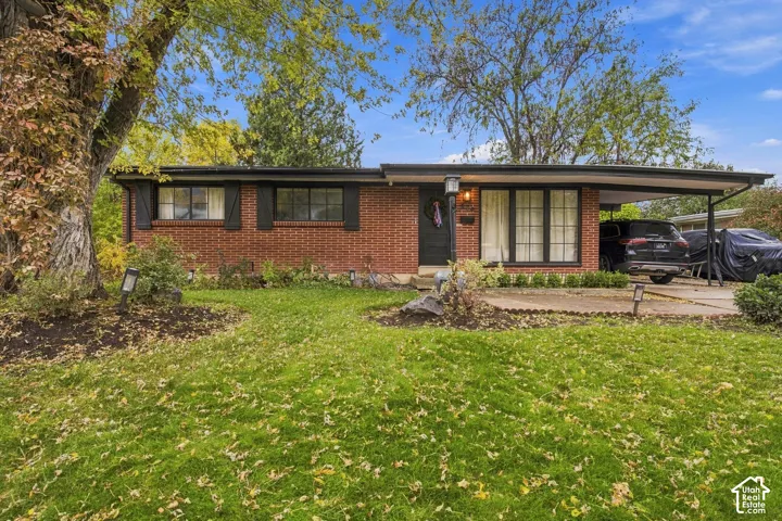 Mid-century modern brick exterior featuring a covered carport, dark-toned window trim, and a prominent mature tree