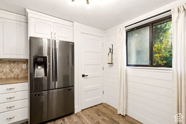 White cabinetry with crown molding, stainless steel French-door refrigerator, diamond-pattern tile backsplash, shiplap wall paneling, and wood-finish flooring