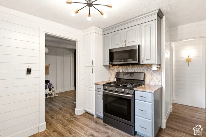 Kitchen featuring painted cabinetry, stone-finish countertops, geometric tile backsplash, stainless steel appliances, and wood-finish flooring