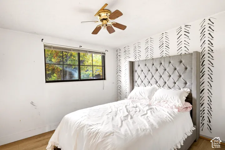 Bedroom interior featuring wood-finish flooring, a multi-pane window, and a ceiling-mounted light fixture with a fan