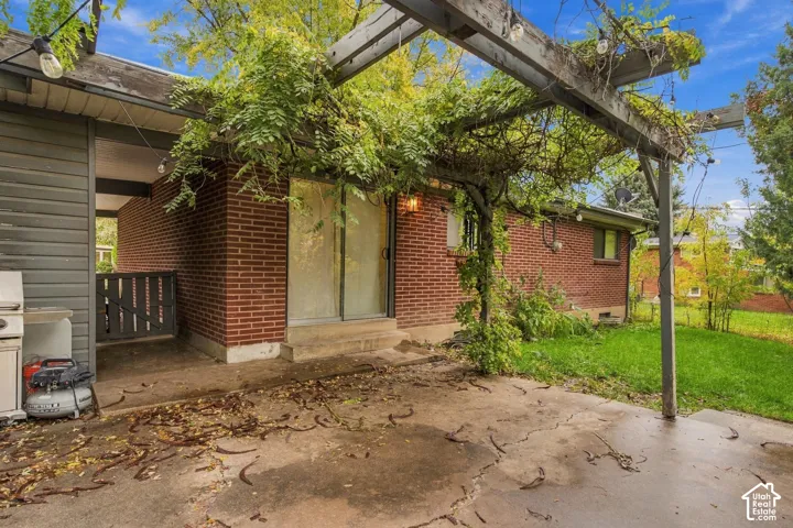 Exterior patio featuring a red brick facade, wood-beam pergola, and sliding glass door