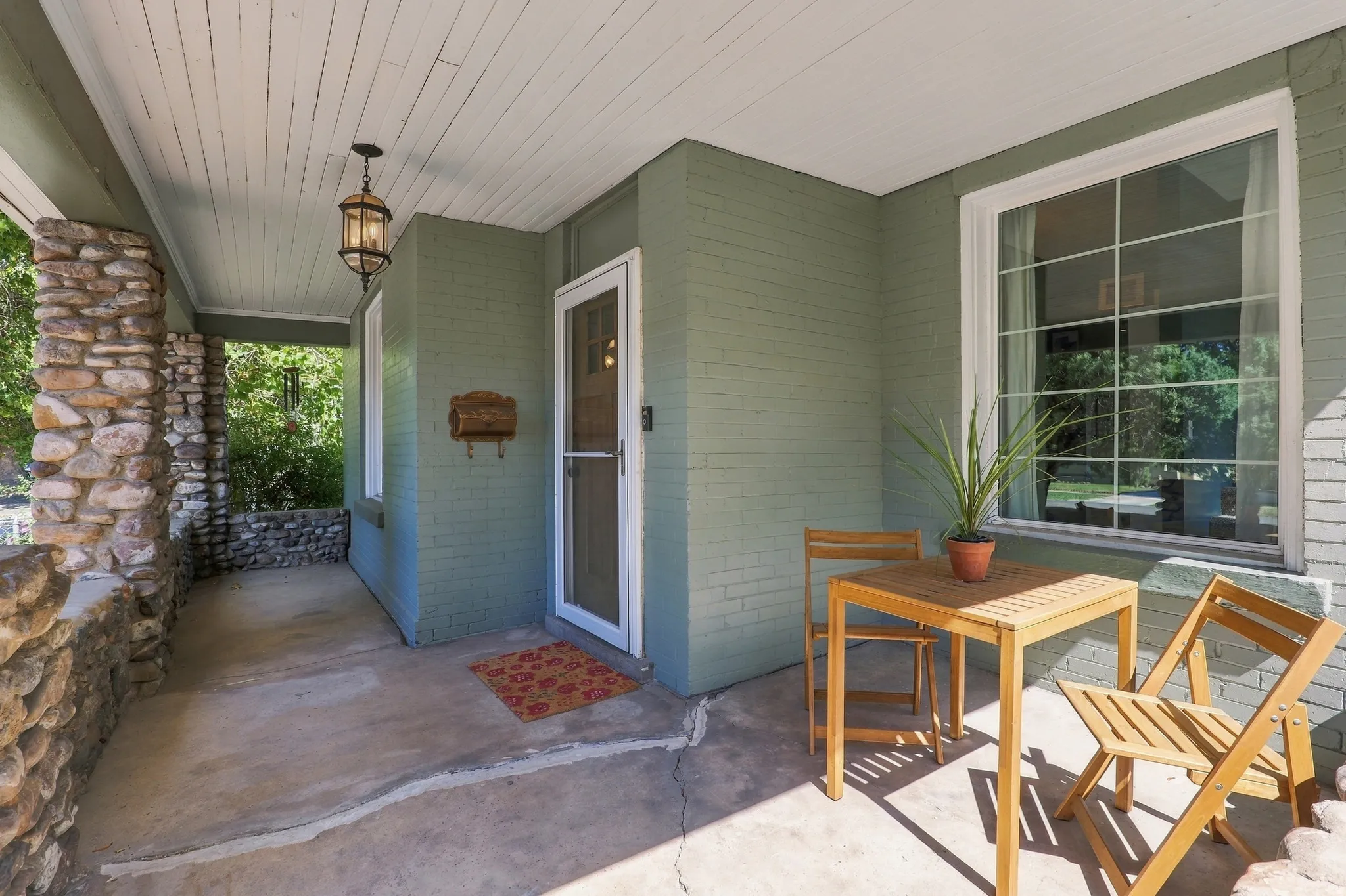 Covered porch featuring stone pillars and a brick wall