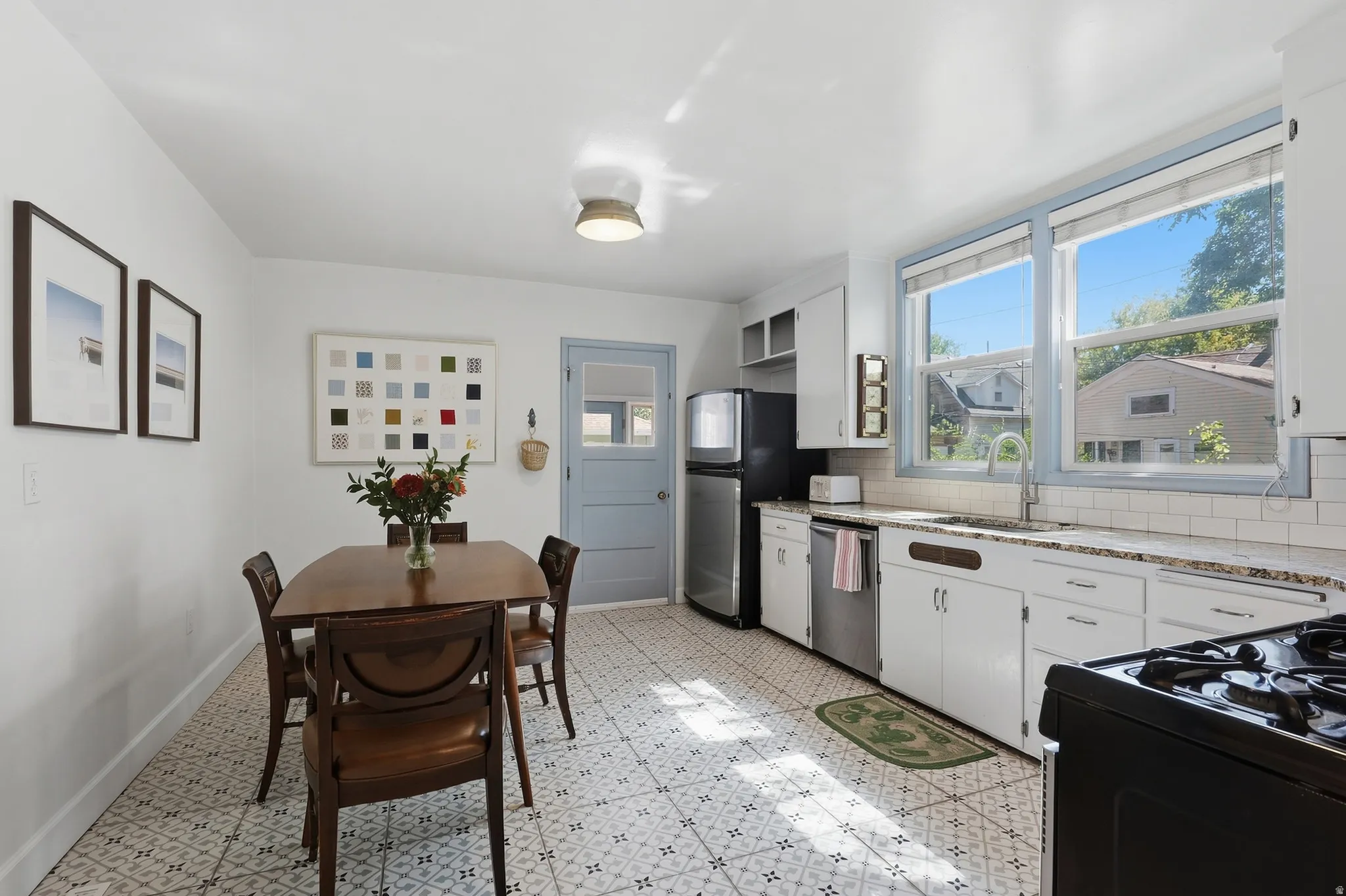 Crisp white cabinetry, wood-finish flooring, white subway tile backsplash, stainless steel appliances, and a light blue door with a glass panel