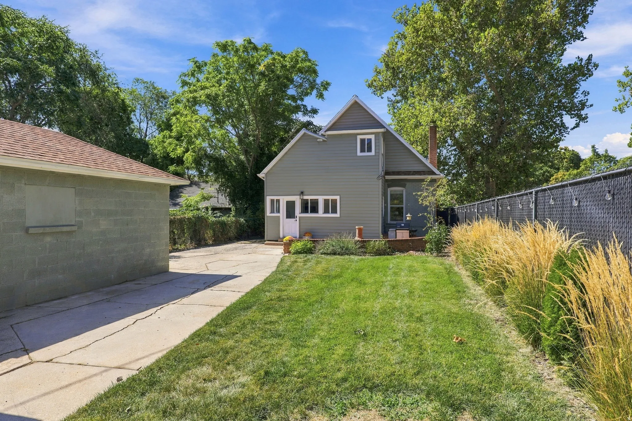 Expansive lawn area, mature perimeter trees, detached garage with shingle roofing, concrete driveway, and a rear deck