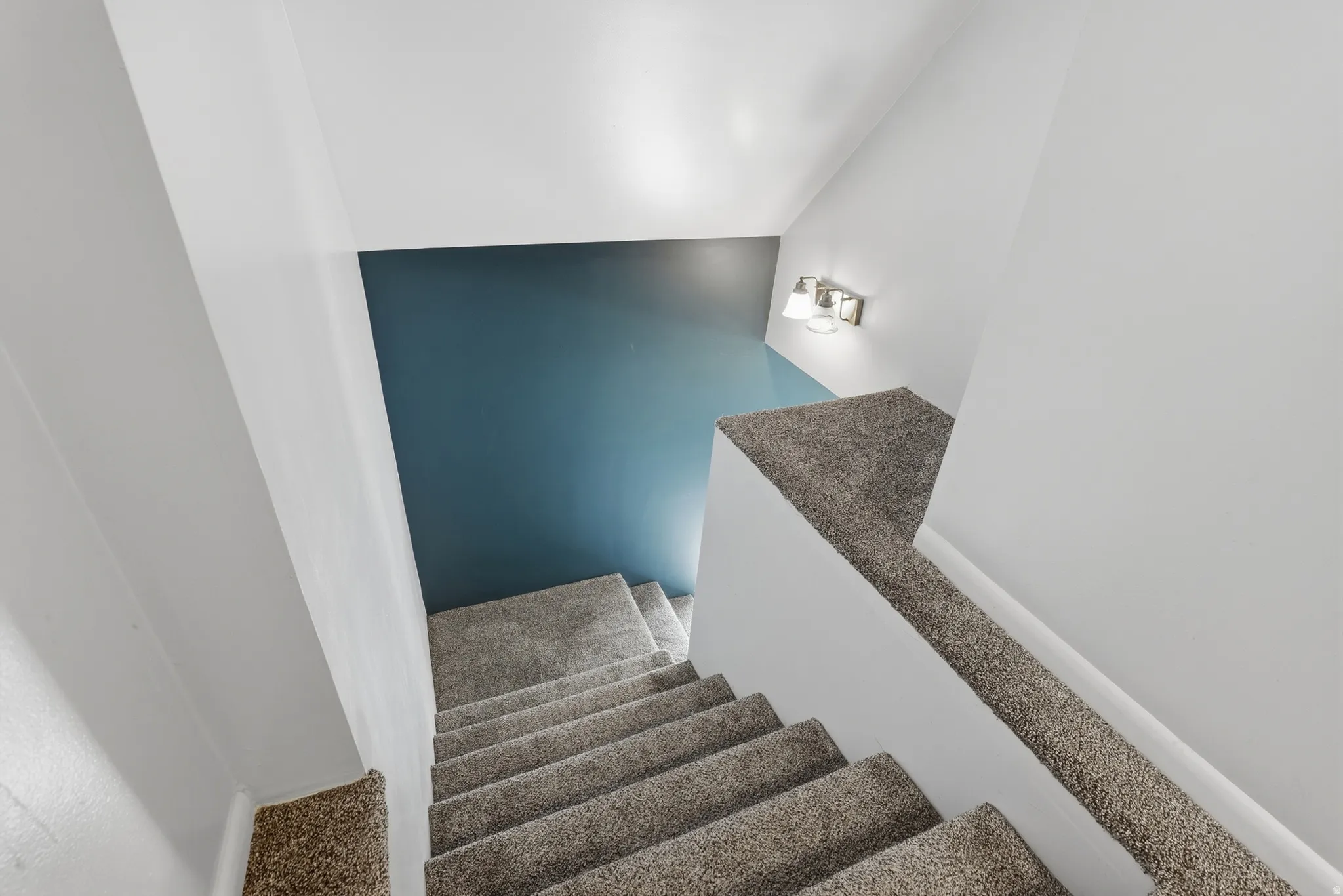 Carpeted staircase with white walls, a single accent wall, and a three-light sconce