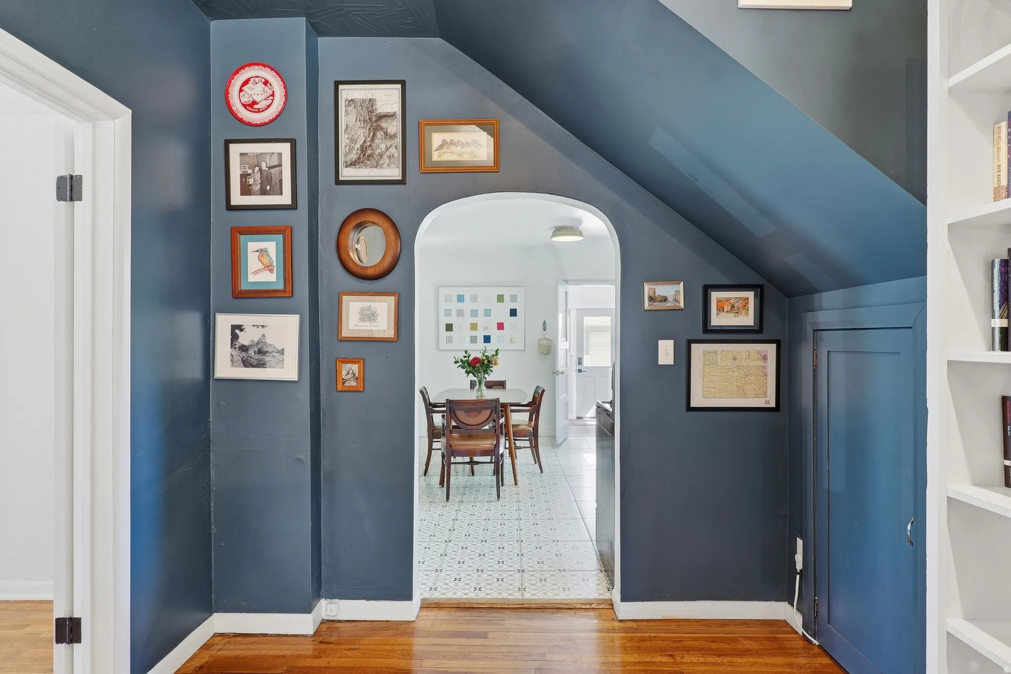 Hardwood flooring, arched doorway, built-in shelving, paneled walls, and white trim