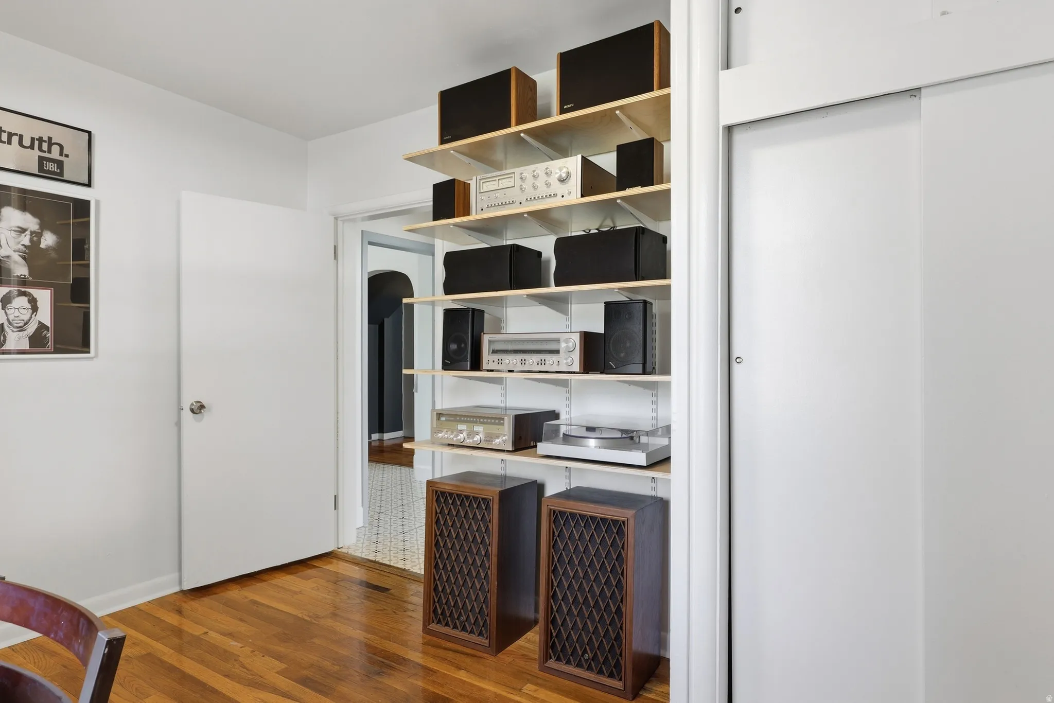 Hardwood flooring, white painted walls, white interior door with chrome hardware, built-in shelving system with wood shelves, and white sliding closet doors