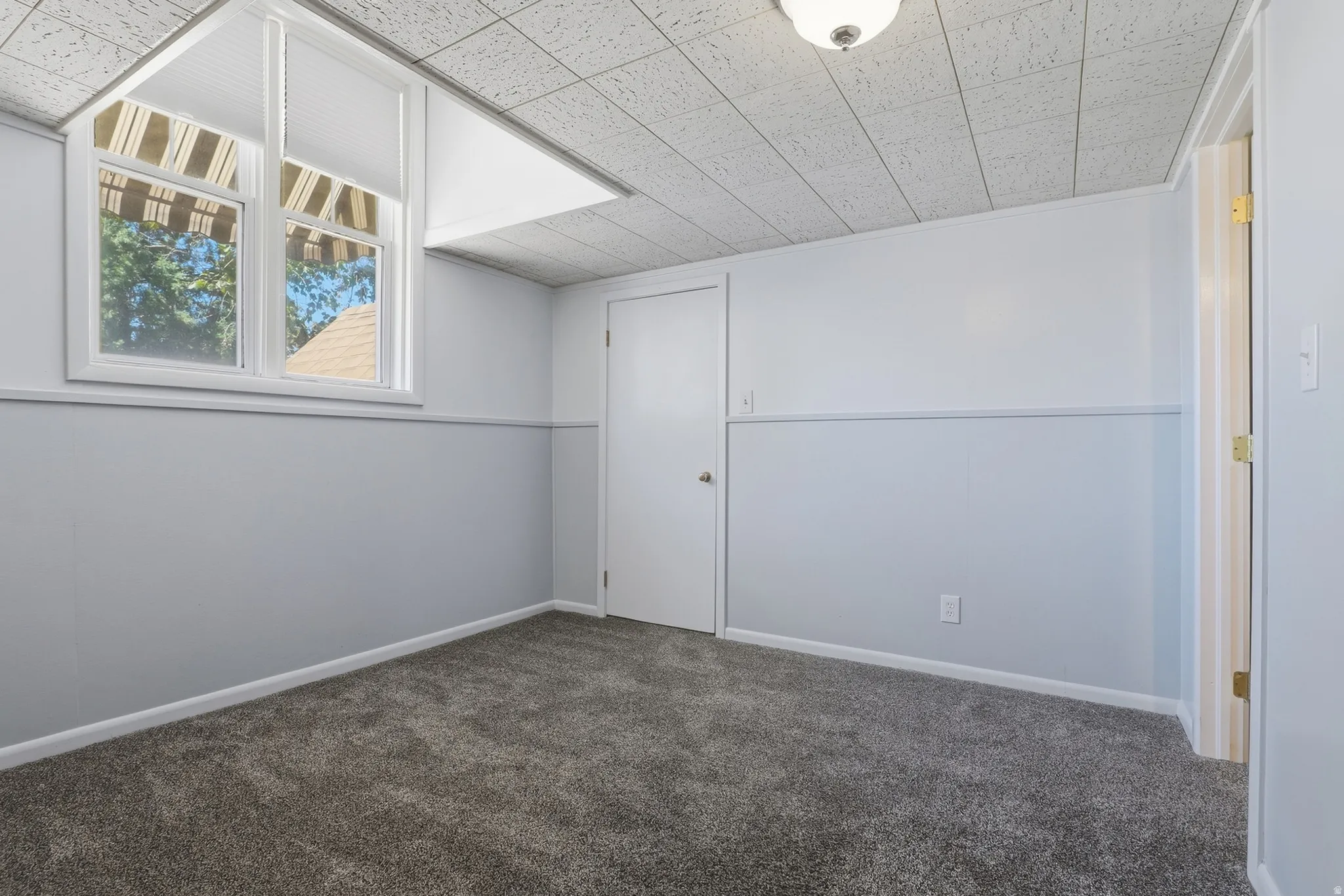 Recessed window with white blinds, wall paneling, white interior doors, textured acoustic ceiling, and neutral carpet