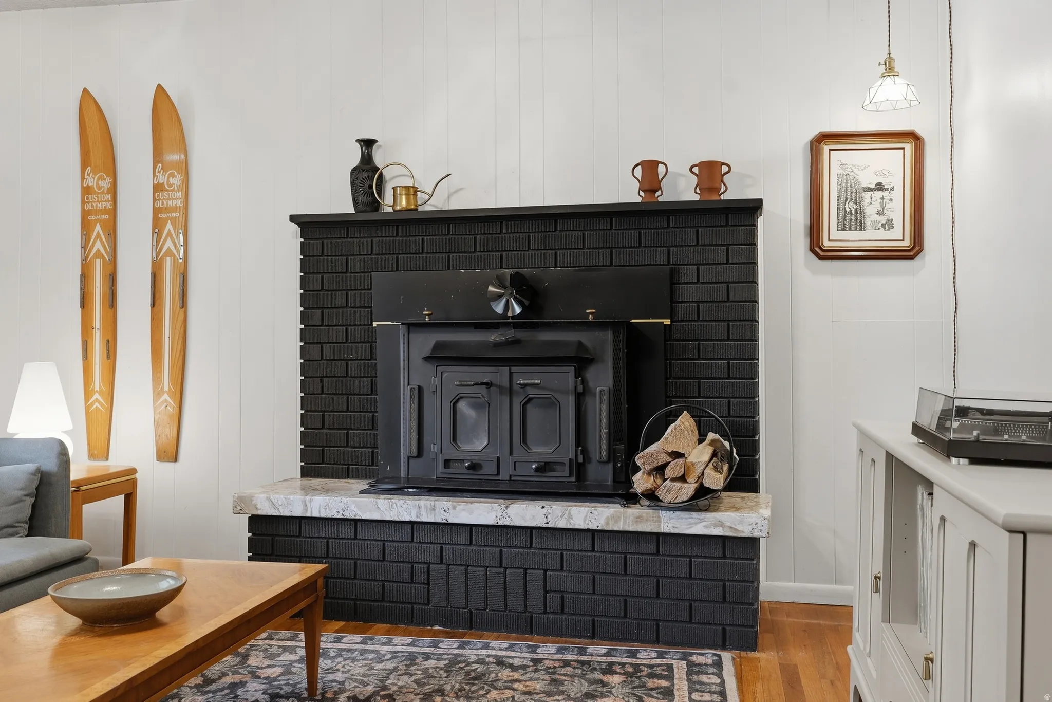 Black brick fireplace with stone hearth, wood-burning insert, and wood-finish flooring