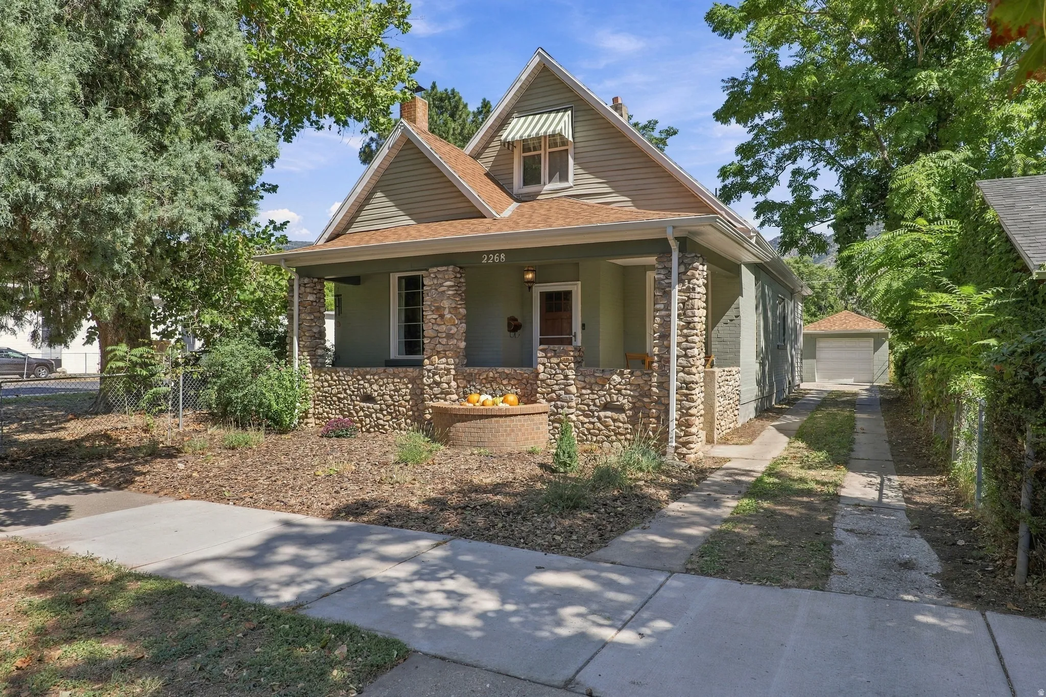 Craftsman-style residence with a covered porch, stone columns, horizontal siding, a gabled roof, and a detached garage