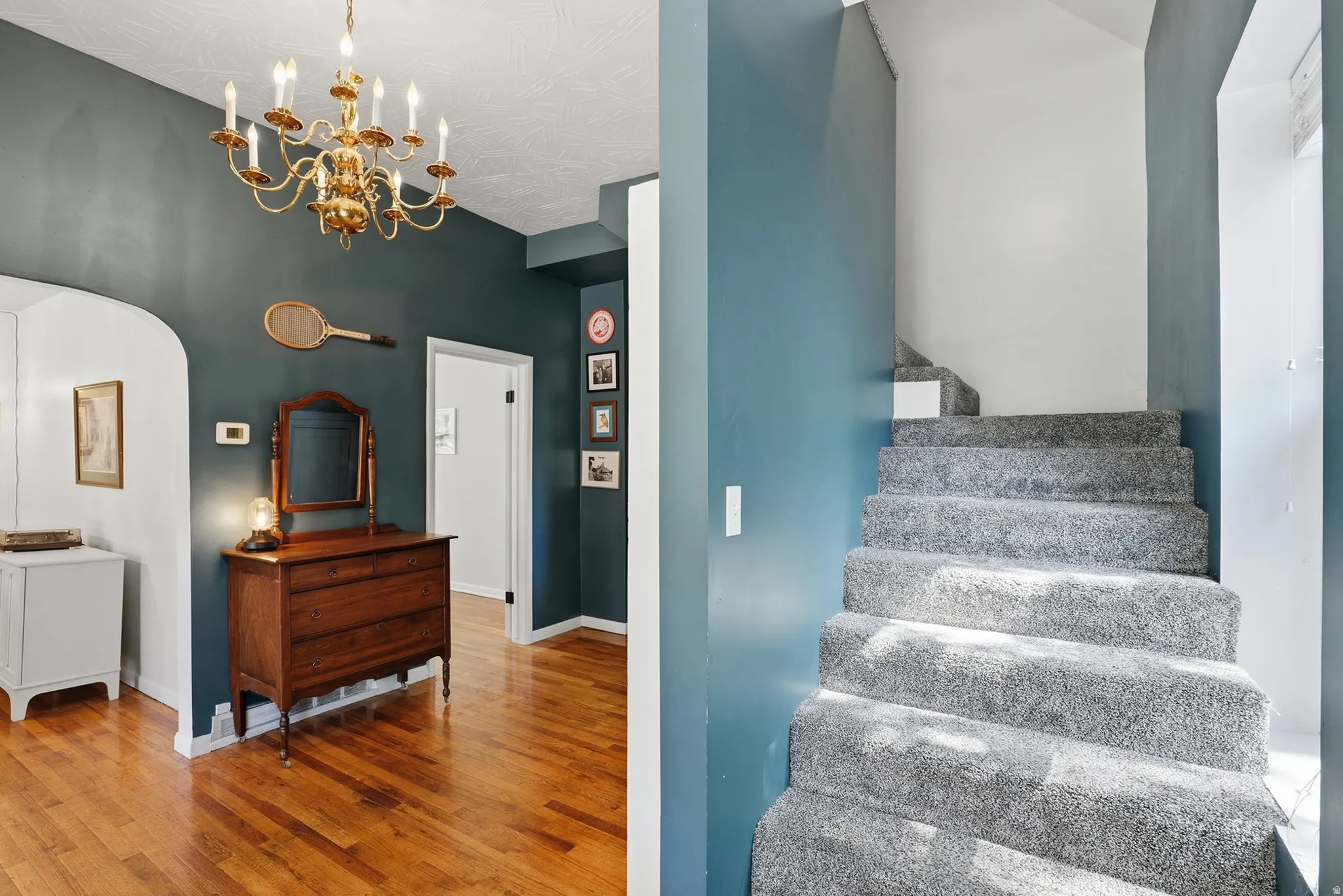 Hardwood flooring, arched doorway, brass chandelier, and carpeted staircase