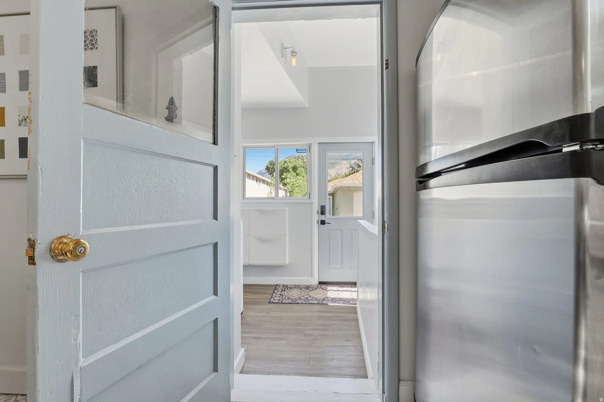 Paneled interior door with a brass knob, wood-finish flooring, and a stainless steel refrigerator