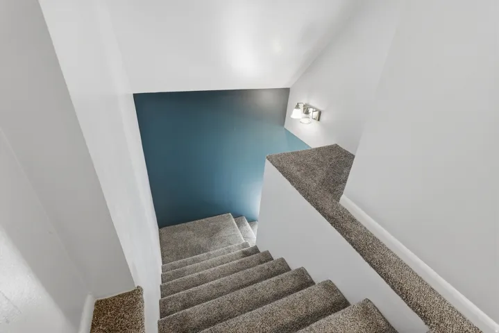 Carpeted staircase with white walls, a single accent wall, and a three-light sconce