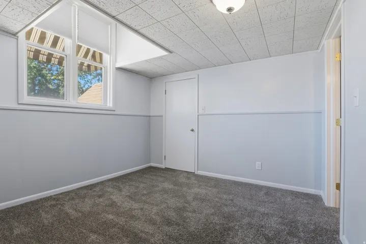 Recessed window with white blinds, wall paneling, white interior doors, textured acoustic ceiling, and neutral carpet
