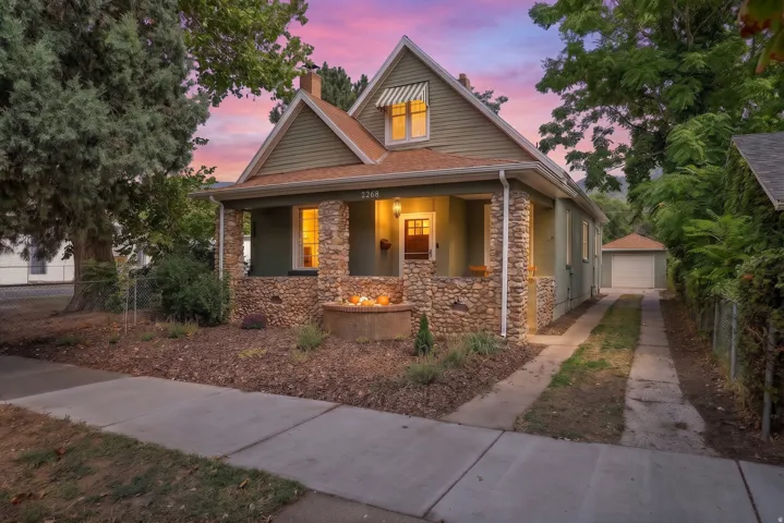 Traditional architecture featuring a stone-clad porch, gabled roof, siding exterior, and a detached garage with a concrete driveway