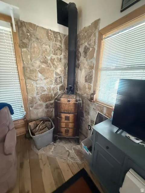 Stone accent wall with a built-in wood-burning stove, wood-finish flooring, and natural wood window trim