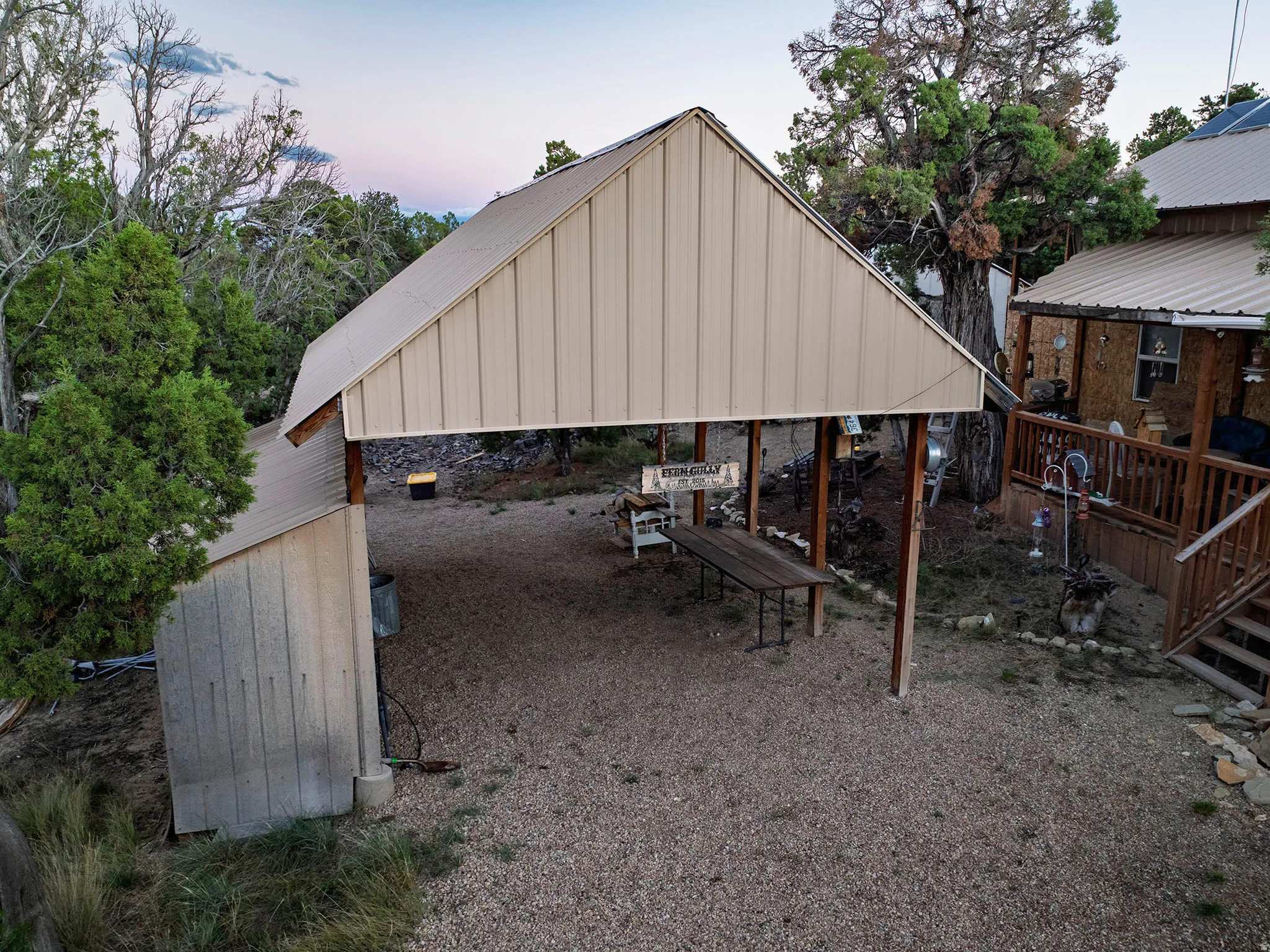 Gravel parking area featuring an attached carport with a metal roof and a separate outbuilding