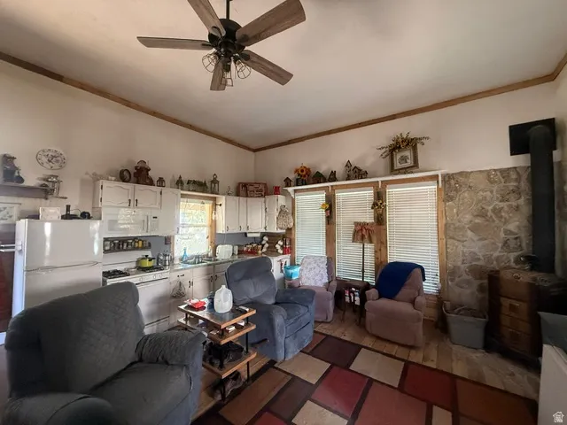 Vaulted ceiling with wood-finish ceiling fan, wood-finish flooring, white cabinetry with integrated appliances, stone accent wall, and multiple windows with blinds