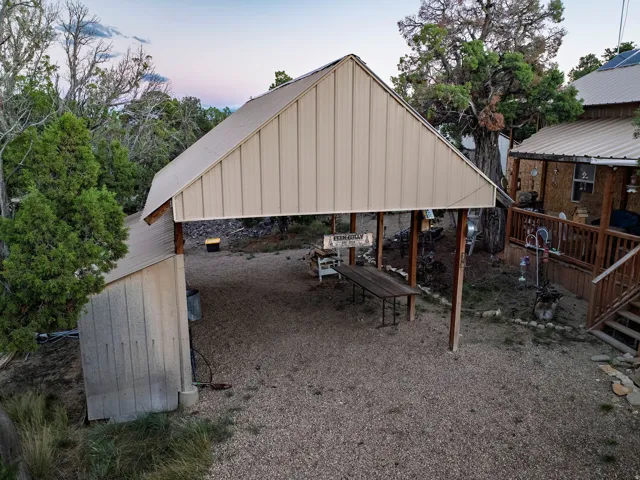 Gravel parking area featuring an attached carport with a metal roof and a separate outbuilding