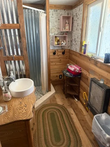 Wood-finish flooring, wood plank walls, and a white vessel sink on a wood vanity