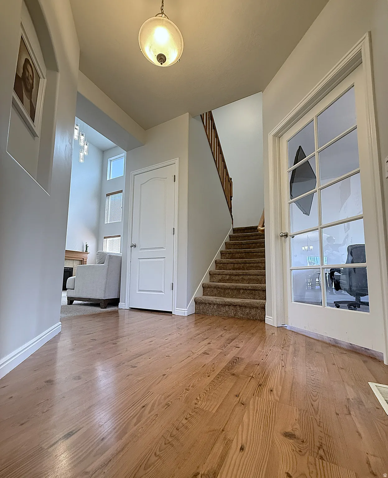 Hardwood-finish flooring, staircase with carpeted treads, white panel doors, overhead light fixture, and a glass-paneled door
