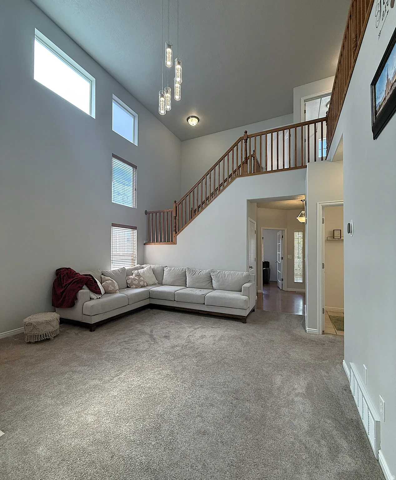 High ceilings with multiple large windows, wood-finish staircase with balusters, and a contemporary multi-light pendant fixture