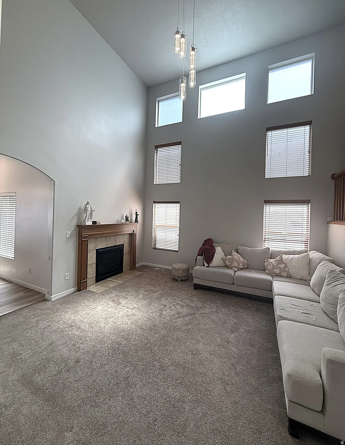 Carpeted living space featuring a fireplace with a wood mantel and tile surround, a high vaulted ceiling, and multiple windows with blinds
