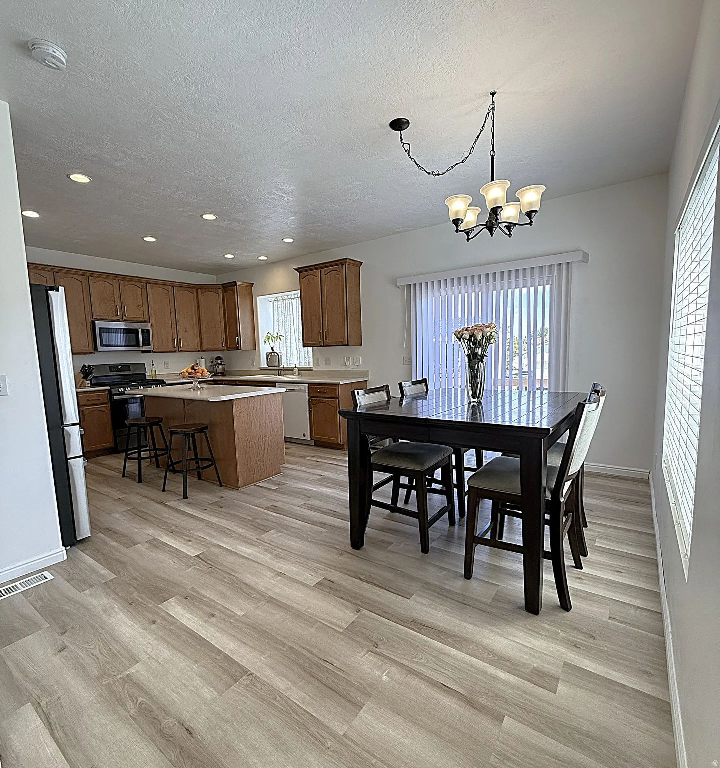 Open-concept kitchen and dining area featuring wood-finish flooring, recessed lighting, and a modern chandelier