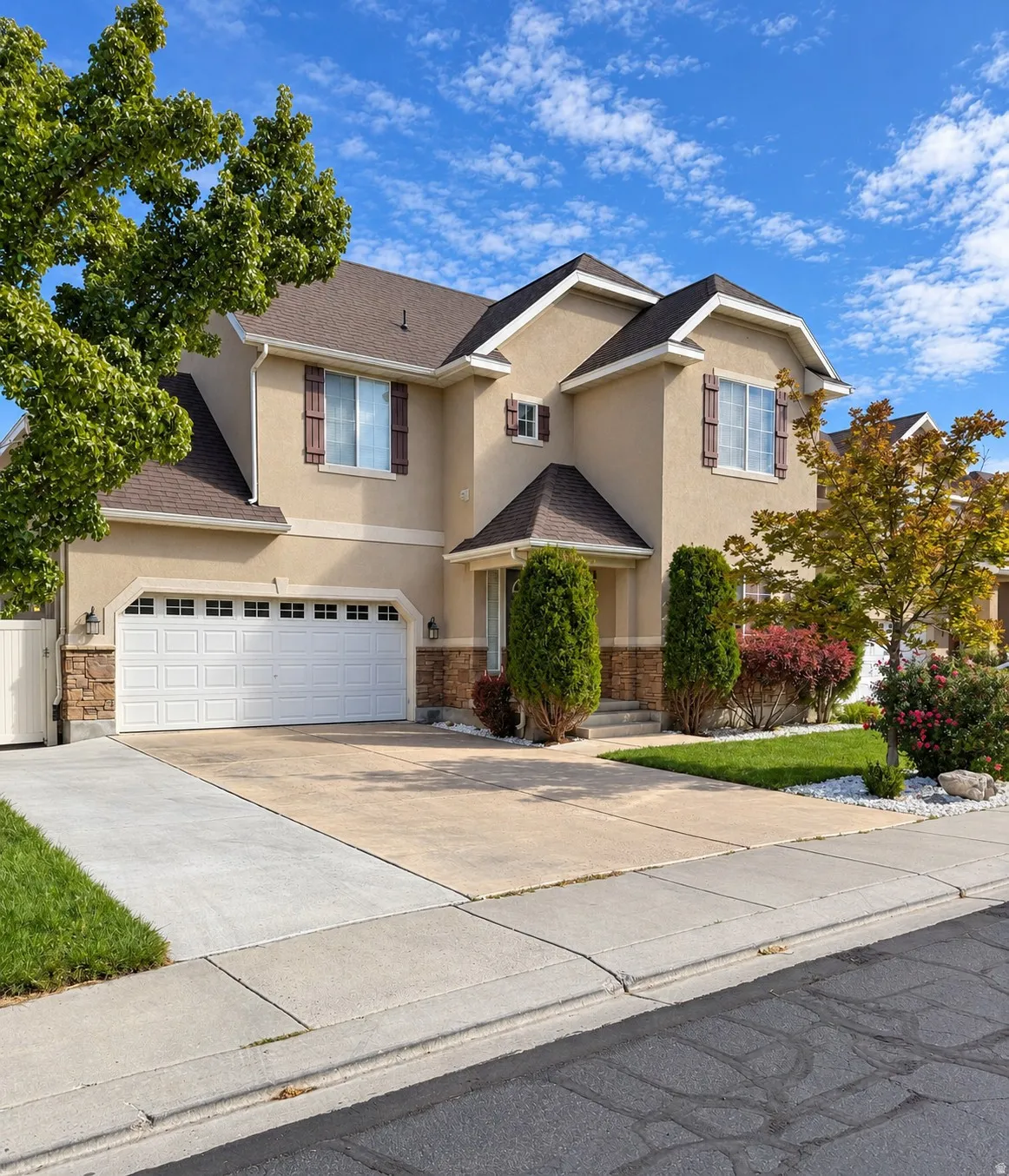 Stucco exterior with stone accents, attached two-car garage, mature landscaping, and a concrete driveway