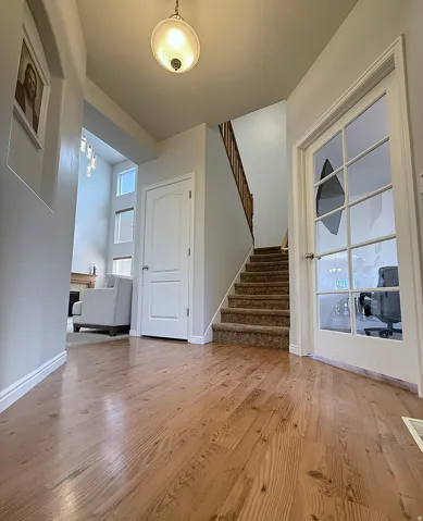 Hardwood-finish flooring, staircase with carpeted treads, white panel doors, overhead light fixture, and a glass-paneled door