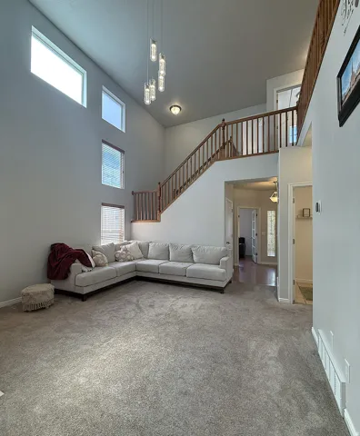 High ceilings with multiple large windows, wood-finish staircase with balusters, and a contemporary multi-light pendant fixture