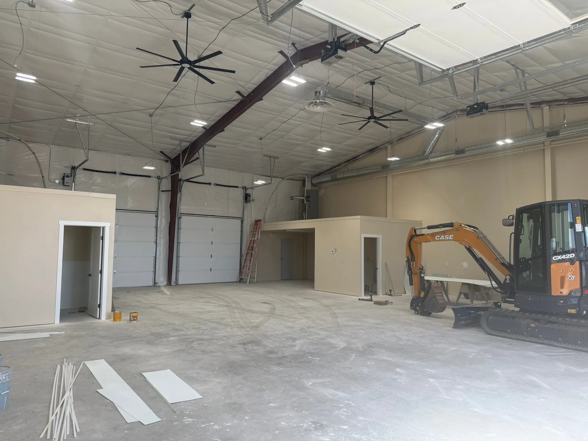 Spacious interior featuring a concrete floor, two large overhead doors, exposed structural beams, and multiple ceiling fans