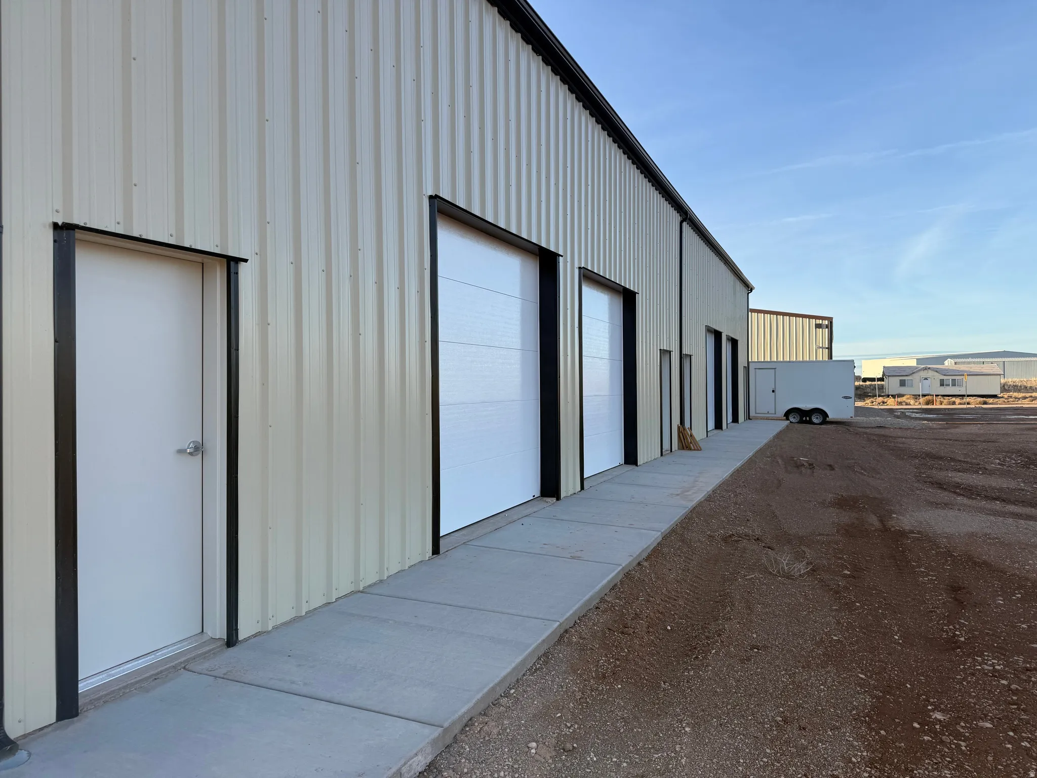 Corrugated metal panel exterior with multiple roll-up garage doors, a concrete walkway, and a flat roofline