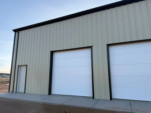 Corrugated metal exterior with black trim, two roll-up garage doors, a single entry door, and concrete pedestrian pathways