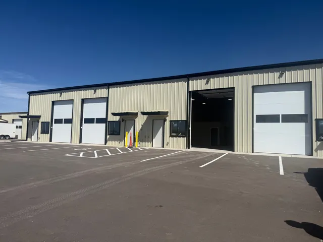 Metal-sided industrial building featuring multiple roll-up doors, individual entry doors, and an asphalt parking lot with painted lines