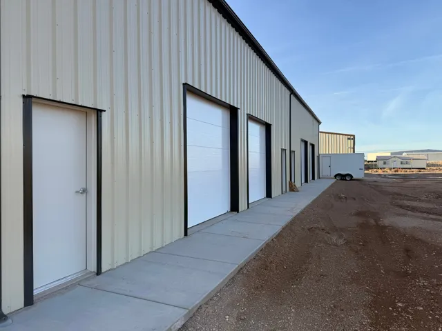 Corrugated metal panel exterior with multiple roll-up garage doors, a concrete walkway, and a flat roofline