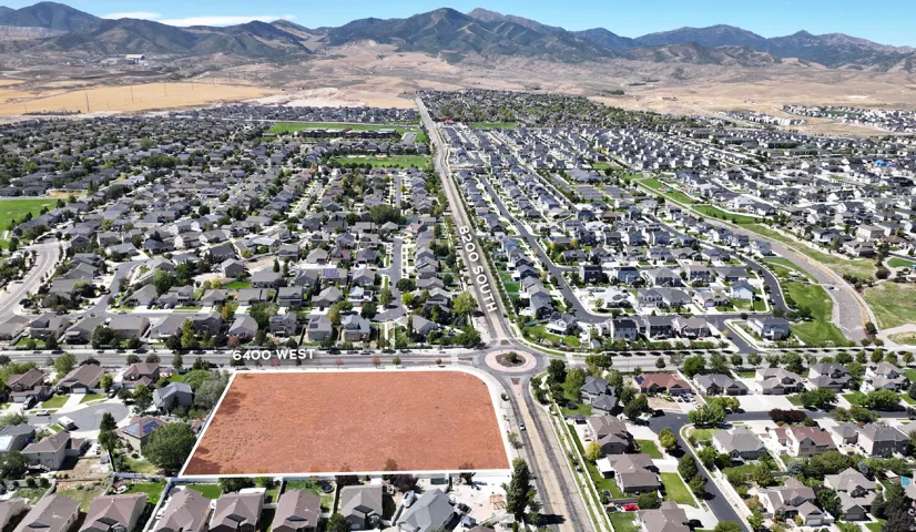Expansive undeveloped parcel with direct road frontage on 6400 West and 8200 South, bordered by established residential areas, and featuring distant mountain scenery