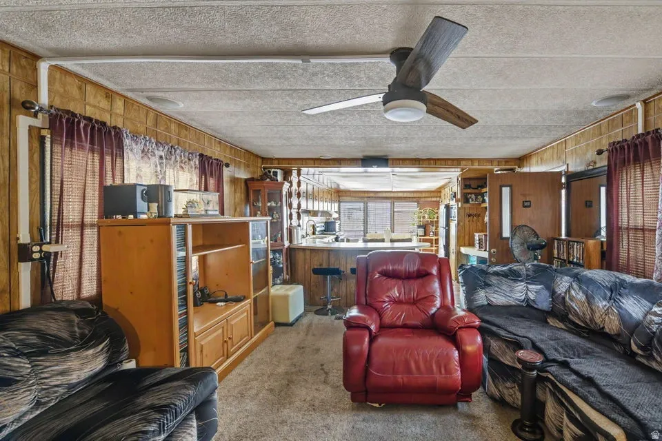 Wood paneling throughout, ceiling fan with light fixture, built-in shelving, window with blinds, carpeted flooring