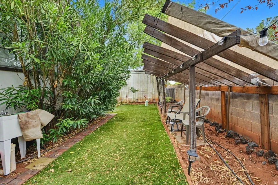 Manicured lawn, mature shrubs, brick border, and a wood-frame pergola with a fabric canopy