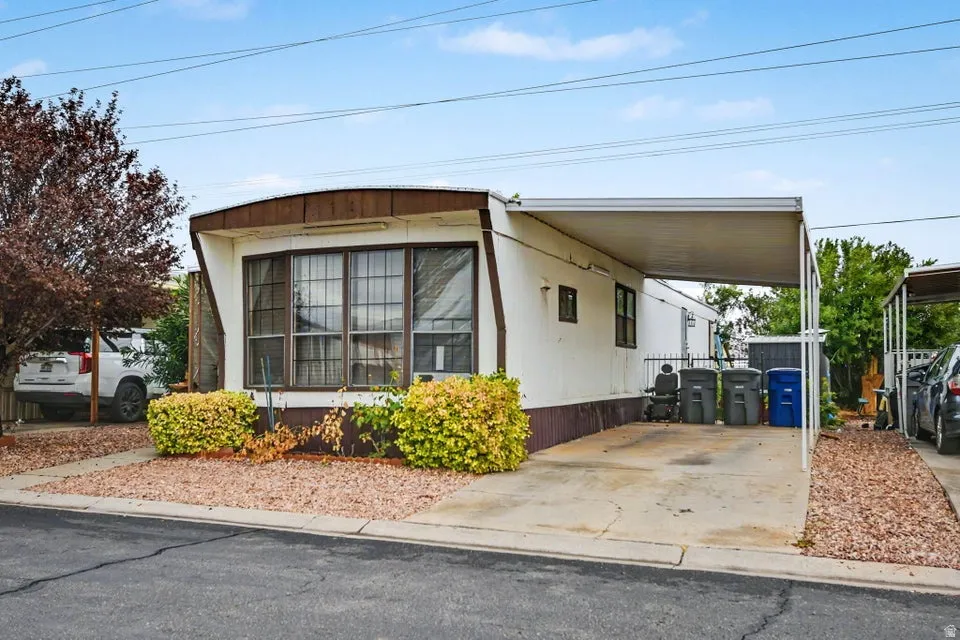 Paved driveway with an attached carport, front landscaping featuring decorative gravel and mature shrubs, and an additional parking area